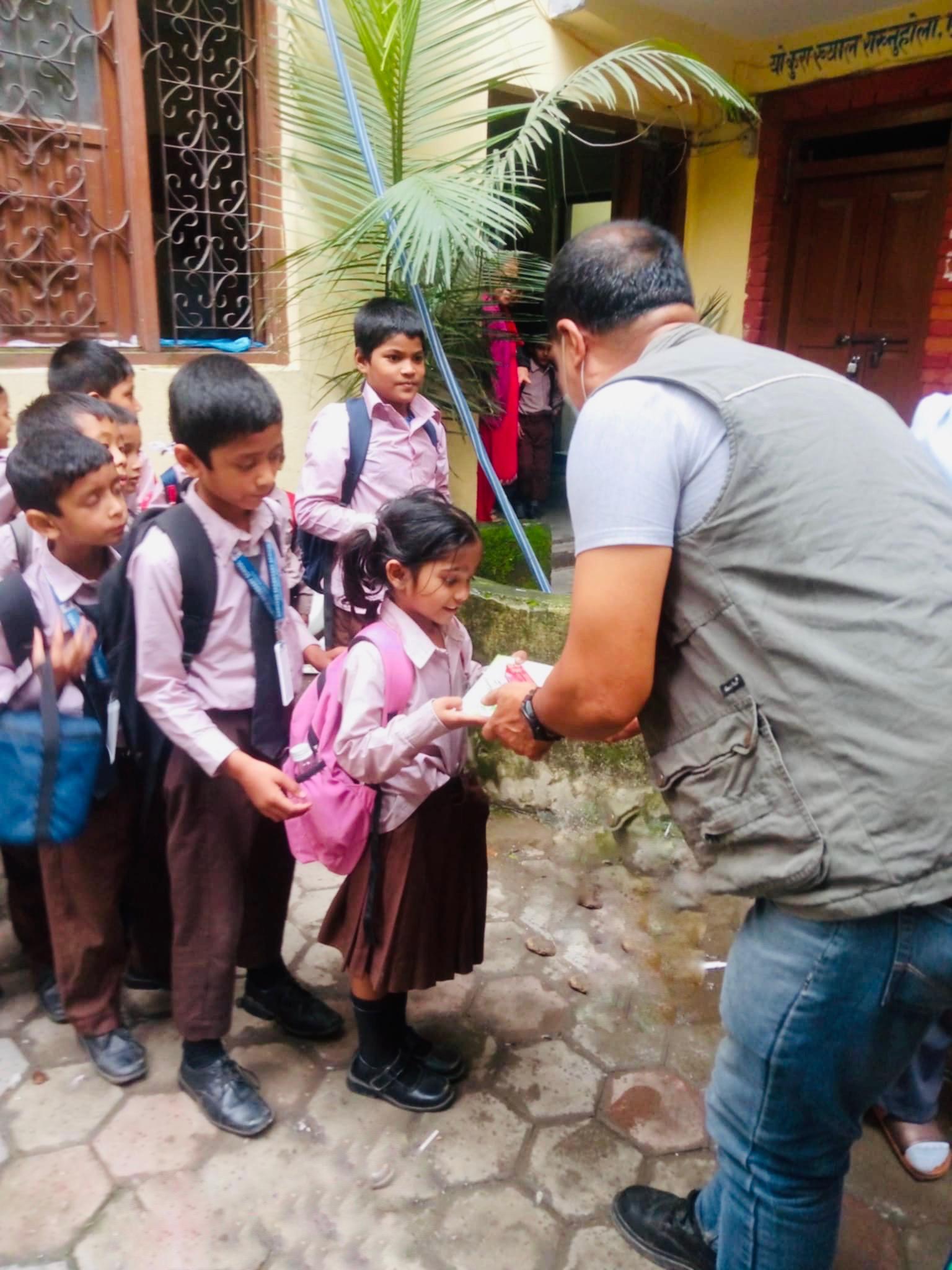 Children gathered around a volunteer distributing supplies outside a school