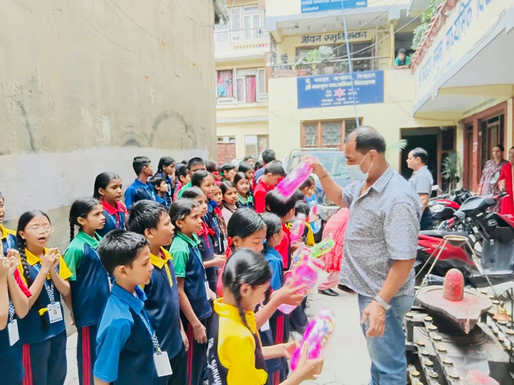 Children holding water bottles and school supplies beside volunteers in a school courtyard