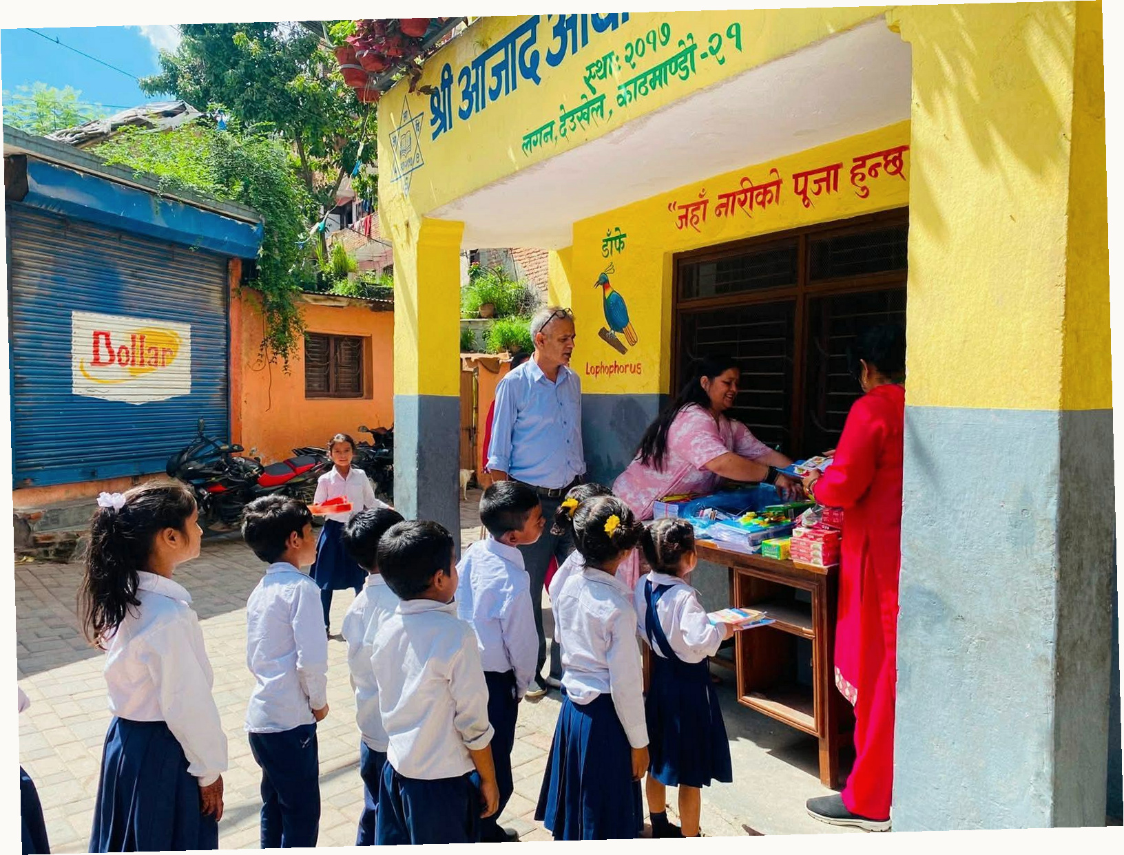 Children and adults distributing school supplies outside a yellow school building